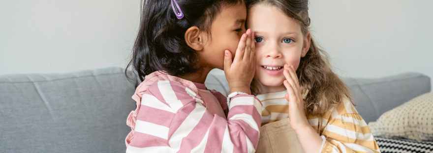 hispanic girl whispering secret on ear of friend