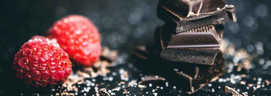 close up photo of stacked chocolates bars beside raspberries